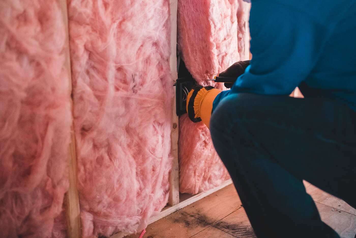 Gloved hands fitting pink insulation between studs