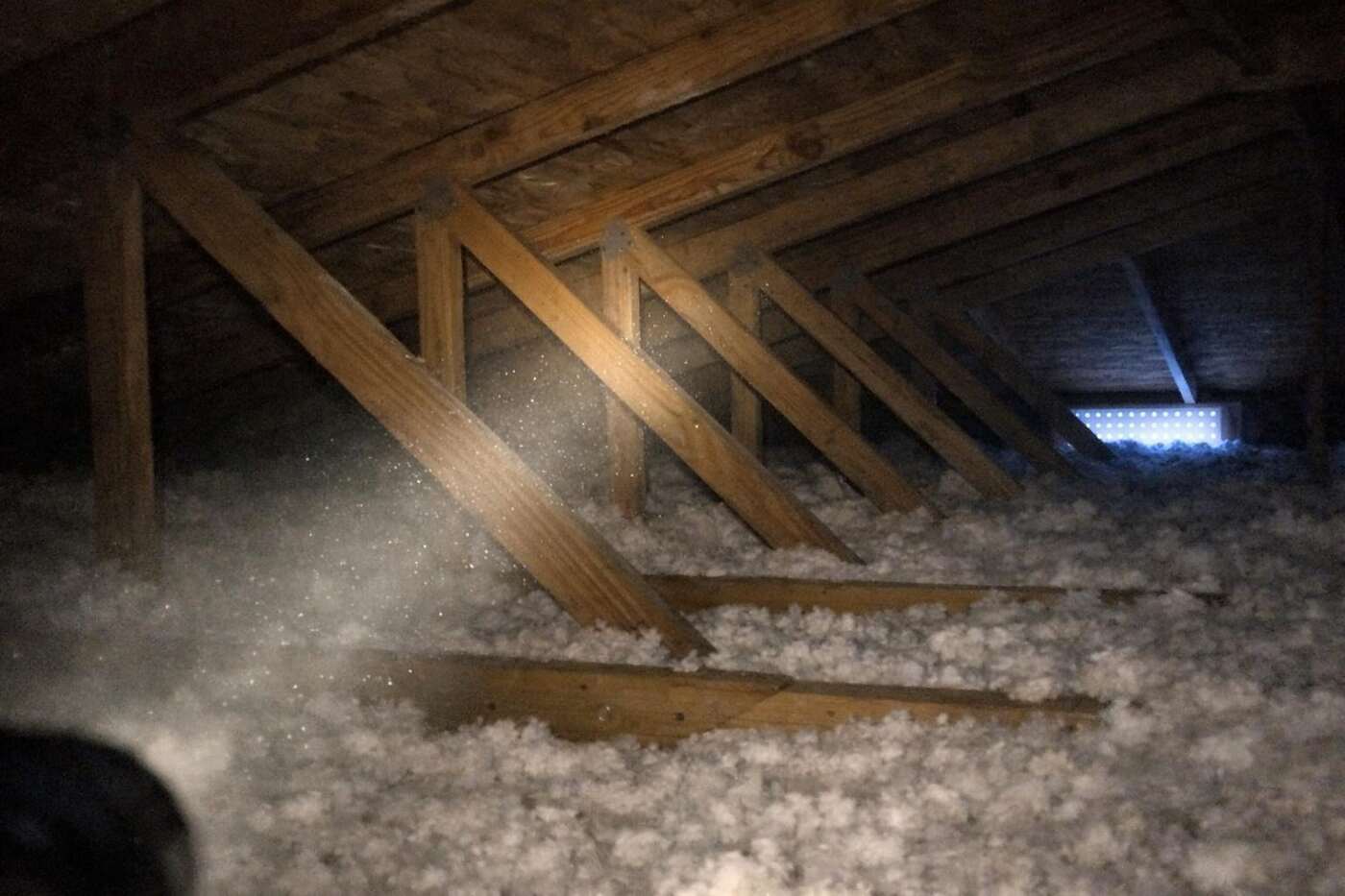 A light across the trusses and insulation of a dim attic