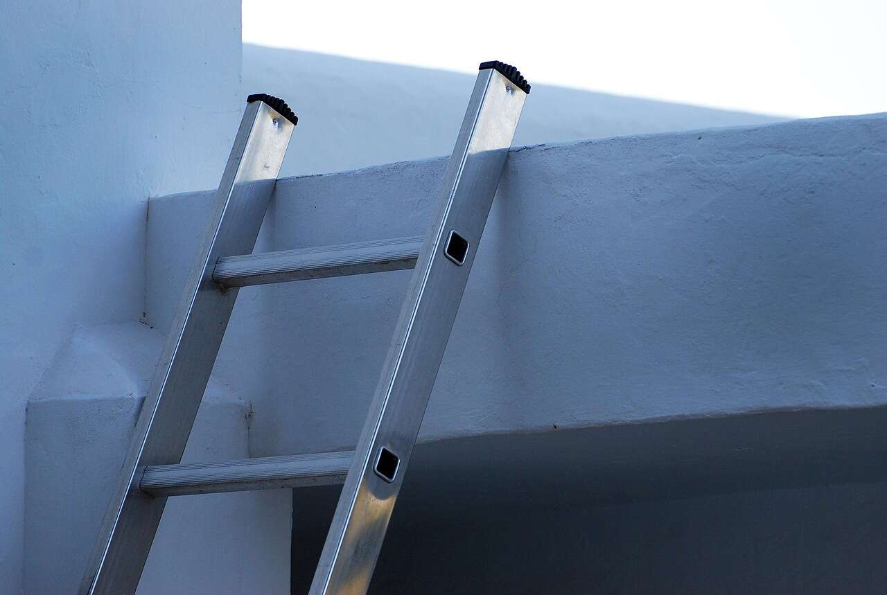 An aluminum ladder leaning against the edge of a roof