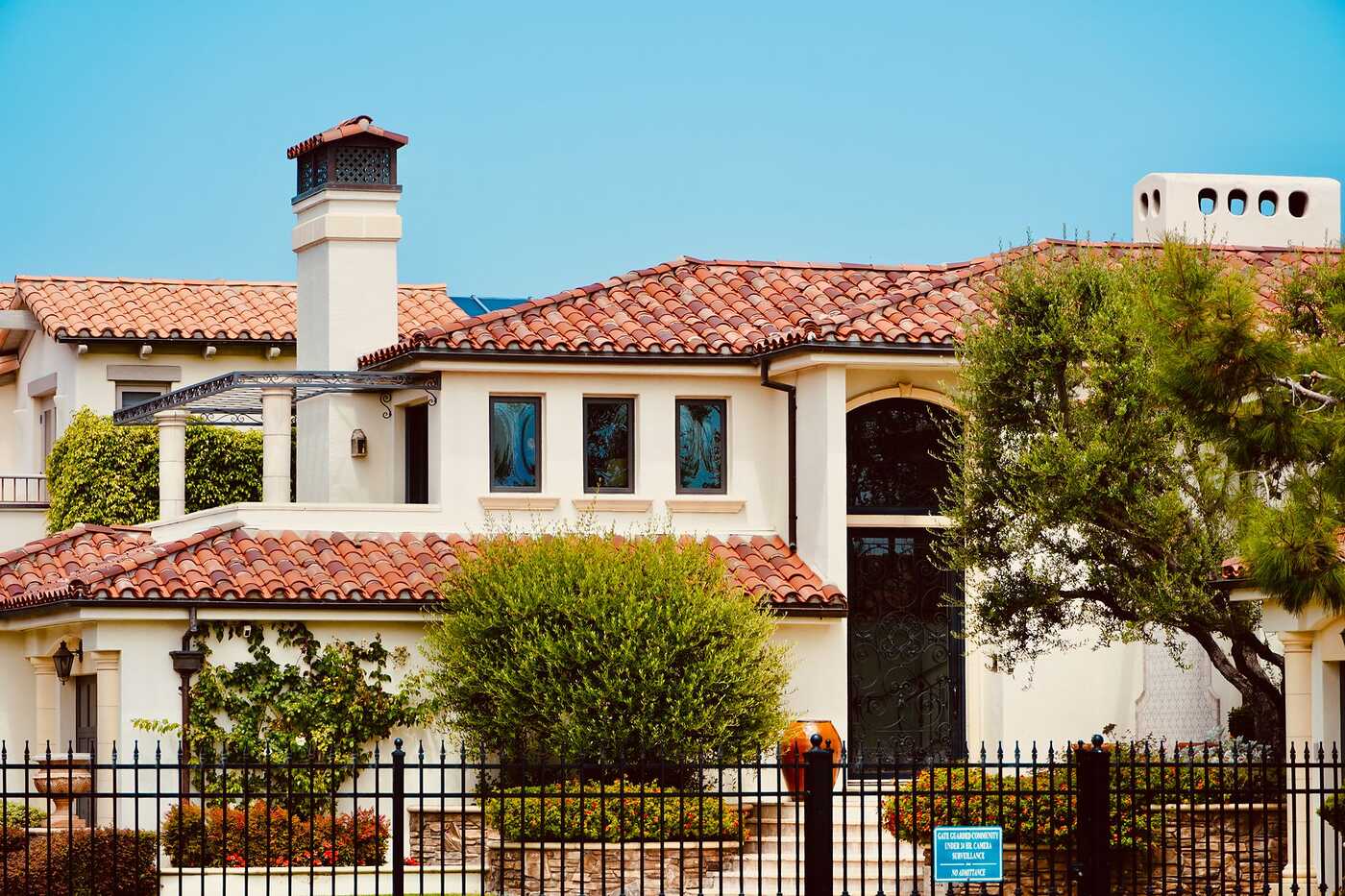 A two-story Mediterranean-style house with a tile roof behind greenery